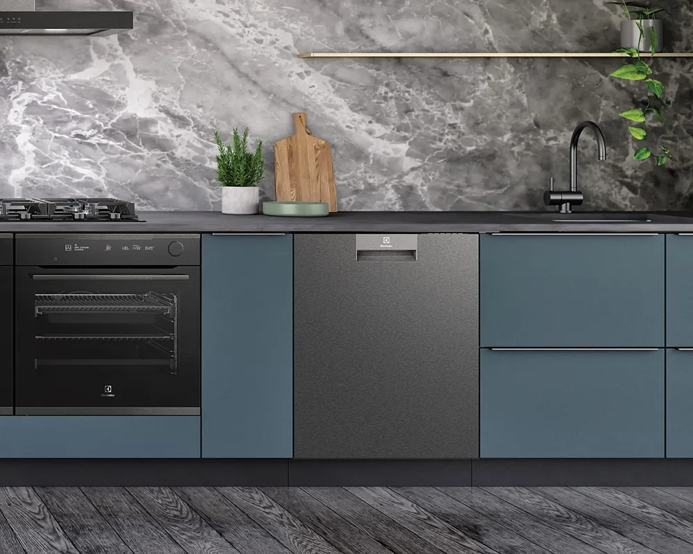 A modern kitchen showcasing an Electrolux dishwasher integrated into blue cabinetry, with an Electrolux oven and gas cooktop on the left, set against a grey marble backsplash with minimal decor